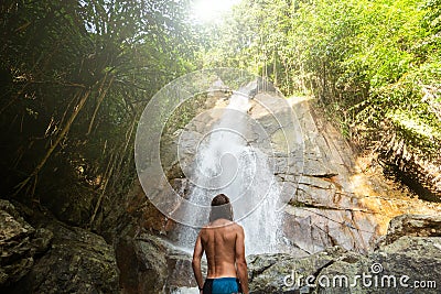 Man with a long hair is enjoy in lagoon of huge tropical waterfall in jungle. Travel concept. Stock Photo