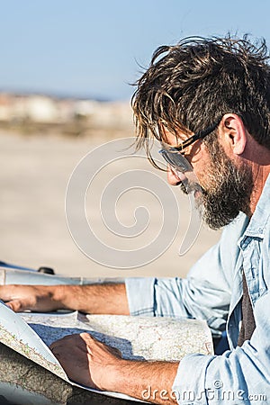 Man look a paper road trip map standing outside the car with blue sky and ground desert in background - concept of travel and Stock Photo