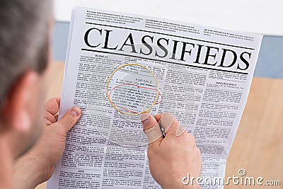 Man looking classifieds through magnifying glass Stock Photo