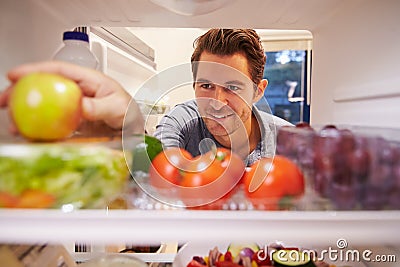 Man Looking Inside Fridge Full Of Food And Choosing Apple Stock Photo