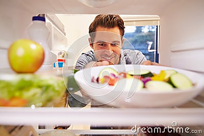 Man Looking Inside Fridge Full Of Food And Choosing Salad Stock Photo