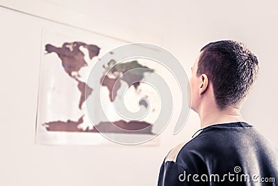 Man looking at a world map on the wall. Thinking about the changing environment, uncertain future or worldwide problems. Stock Photo