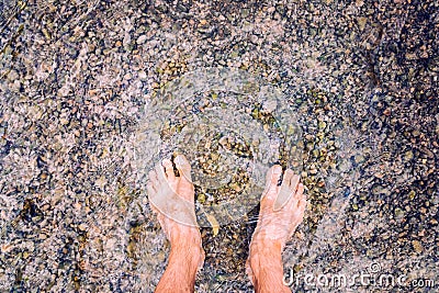 Man looks at his feet submerged in the water of a river on the pebbles Stock Photo