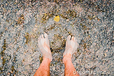 Man looks at his feet submerged in the water of a river on the pebbles Stock Photo