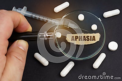 A man looks through a magnifying glass at pills, a syringe and a piece of paper with the inscription - Aphasia Stock Photo