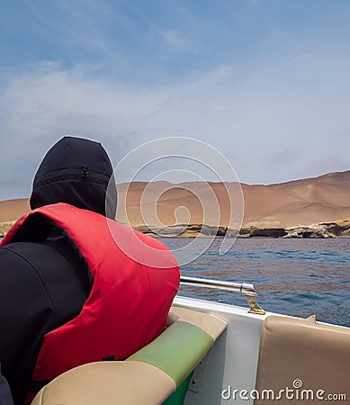 Man lost in thought admires the view, is wearing a life jacket inside a boat, sand dune on the background, and the sea Stock Photo