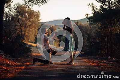 Man in love proposing a surprised, shocked woman to marry him at sunset. Proposal, engagement and wedding concept. Betrothal Stock Photo