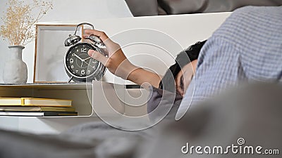 Man lying on bed and extend hand reaching to turn off alarm clock switch. Stock Photo