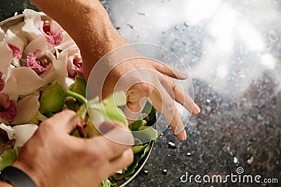 Man making flowers arrangment with green and white orhids Stock Photo