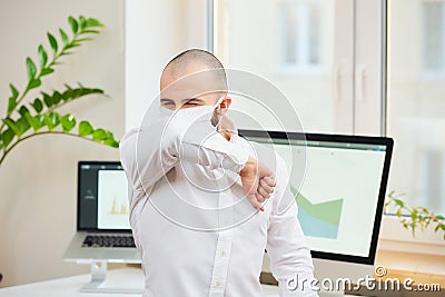 A man in a face mask against the coronavirus coughing in the bend of his elbow Stock Photo