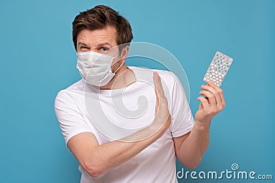 Man in medical mask with pills has a sore throat pointing on them and showing refusing gesture Stock Photo