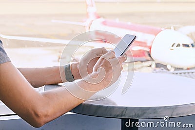 Man on mobile phone waiting for his flight at airport. Male hands holding smartphone, airplane blurry background. Stock Photo