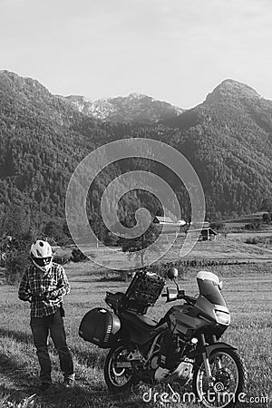 Man motorcyclist Looking for something in the trunk. Alpine mountains on background. Biker lifestyle, world traveler. Summer day. Stock Photo