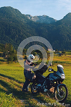 Man motorcyclist Looking for something in the trunk. Alpine mountains on background. Biker lifestyle, world traveler. Summer sunny Stock Photo