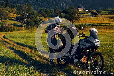 Man motorcyclist Looking for something in the trunk. Alpine mountains on background. Biker lifestyle, world traveler. Summer sunny Stock Photo