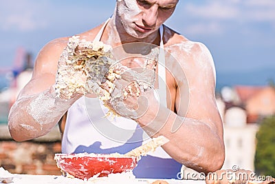 Man muscular baker or cook kneading dough in bowl. Hands of chef cook covered with sticky dough and flour. Bakery Stock Photo