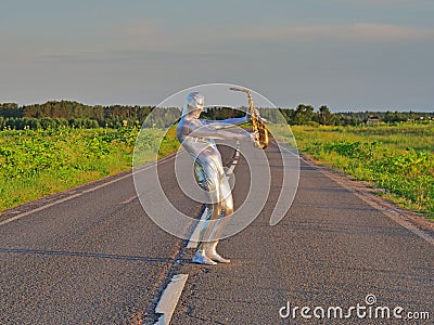 Man musician saxophonist in full body-hugging silver and silver electric suit holding golden alto saxophone, standing on empty Stock Photo