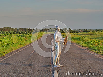 Man musician saxophonist in full body-hugging silver and silver electric suit holding golden alto saxophone, standing on empty Stock Photo