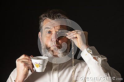 Man with muttonchops and funny expression holding monacle and cup of tea Stock Photo