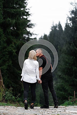 A man next to a woman, guy and a girl are standing close, touching each other, holding hand on forest background. Boy Stock Photo