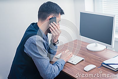 Man in office on telephone using computer and typing on keyboard Stock Photo