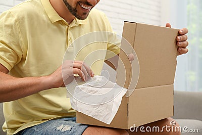 Happy man opening parcel on sofa at home, closeup. Internet shopping Stock Photo