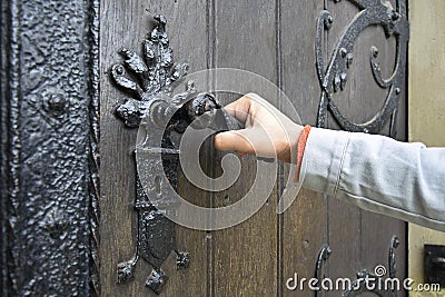 Man opens an ancient wooden door decorated with wrought iron elements Stock Photo