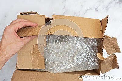 Man opens a damaged and torn cardboard box to transport things. Top view. Bubble wrap keeps things and utensils in Stock Photo