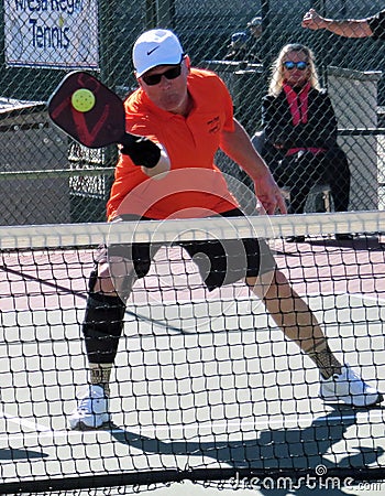 Man in orange shirt and white cap Showing skills in Pickleball Tournament Editorial Stock Photo