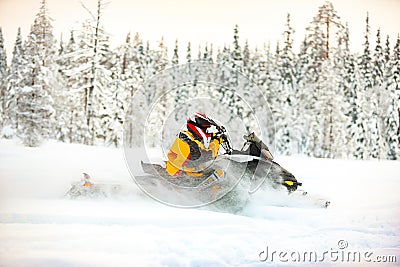 Human in the outfit of a racer in a multi-color jumpsuit and a helmet, driving a snowmobile by the deep snow surface on background Stock Photo