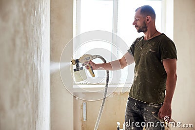Man painting with airbrush apartment repairment against small window in the daytime Stock Photo