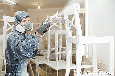 Man painting chair into white paint in respiratory mask. Application of flame retardant ensuring fire protection Stock Photo