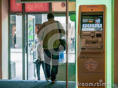 A man passing by yellow terminal with the Tinkoff Bank logo. ATM at the entrance to the mall. Visitors at door Editorial Stock Photo