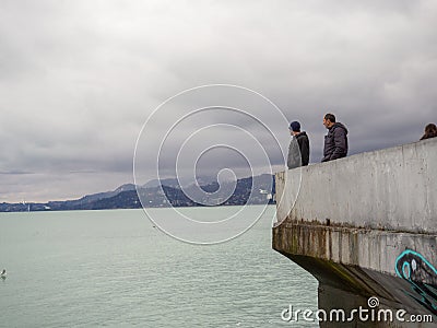 Man on the pier against the backdrop of seagulls. People feed the seagulls. Birds on the sea. Beautiful seascape in cloudy weather Editorial Stock Photo