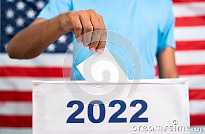 Man placing ballot paper into 2022 ballot box in front of american flag - concept of 2022 midterm US election, voting Stock Photo
