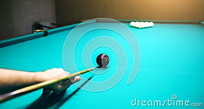 Man is playing billiard. Guy is holding pool cue in his hand. Small black cue ball is on the centre of the green table. Sports and Stock Photo