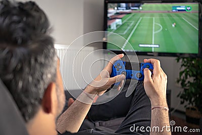 Man playing video game at home sitting on coach sofa in front of television with play game concole and joystick in hands Stock Photo