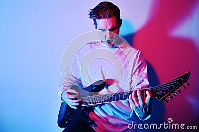 A man plays the electric guitar in neon light, red blue light. Hobbies, music, club. A man enjoys playing the guitar, screaming, Stock Photo