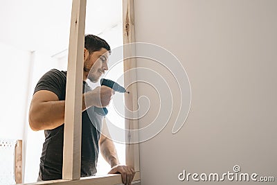 The man is pleased with the screwdriver, fixing the wooden frame for the window to the light wall. Repair yourself Stock Photo