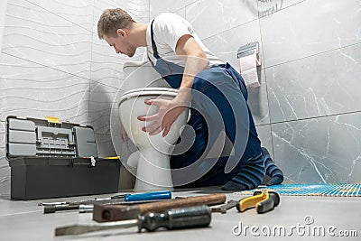 Man plumber in uniform installing toilet bowl using instrument kit professional repair service Stock Photo