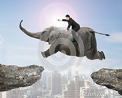 Man with pointing finger riding elephant flying over two cliffs Stock Photo