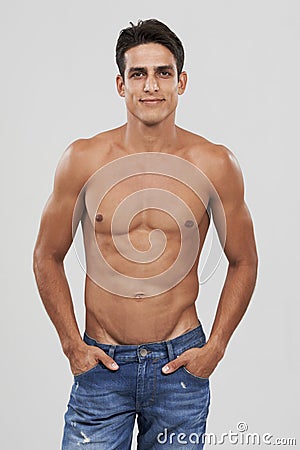 Man, portrait and confident in studio for fashion, smiling and bodybuilder in jeans for style. Male person, shirtless Stock Photo