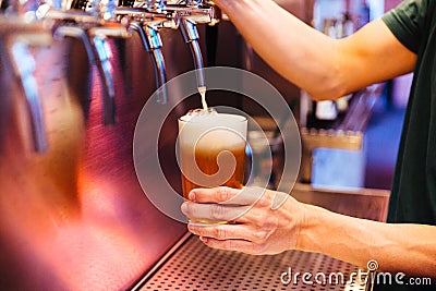 Man pouring craft beer from beer taps in frozen glass with froth. Selective focus. Alcohol concept. Vintage style. Beer craft. Stock Photo