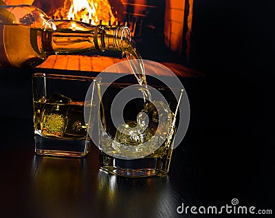 Man pouring glasses of whiskey with ice cubes in front of the fireplace Stock Photo