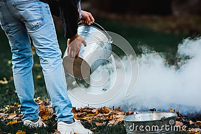 Man pours water from a bucket a bonfire on the grass Stock Photo