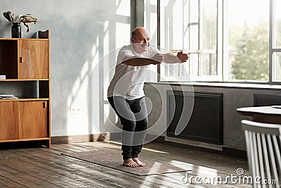 Man practicing yoga indoors at living room doing Chair pose or Utkatasana Stock Photo