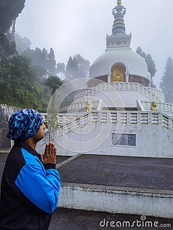 Man praying at buddhist shanti stupa covered with misty fog at morning from different angle Stock Photo