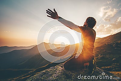 Man praying at sunset mountains raised hands Stock Photo