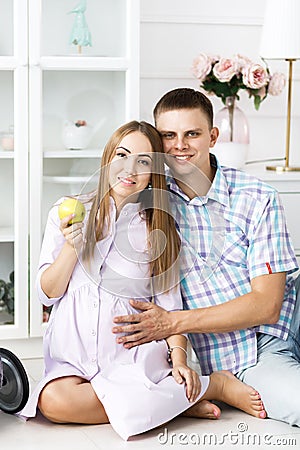 A man and a pregnant woman spend time together, hold apple and sit on the floor. Beautiful bright guest room Stock Photo