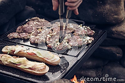 Man prepares a juicy pork neck with basil and barbecue spices and a baguette with tomato cheese and ham on a hot granite slab. Stock Photo